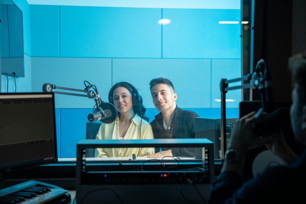 Two people in a radio studio broadcasting a show, featuring professional equipment and microphones with a blue theme.